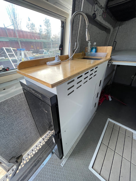 RV rental interior showing a modern kitchenette with a wooden countertop, sink, and built-in refrigerator.
