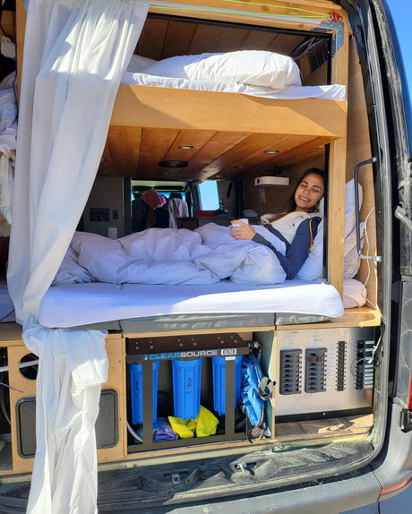 Cozy RV rental with custom bunk beds. A smiling woman enjoys the lower bunk, featuring a water filtration system.