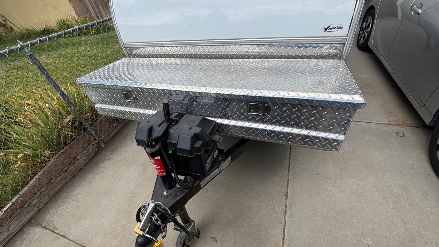 Front of a teardrop RV rental, showing a shiny diamond plate storage box and battery on the hitch. Ready for your travels!