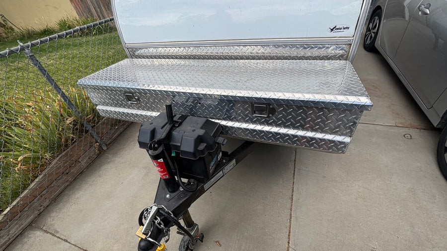 Front of a teardrop RV rental, showing a shiny diamond plate storage box and battery on the hitch. Ready for your travels!