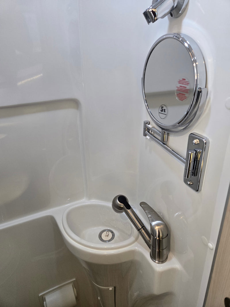 Compact RV rental bathroom with a sink, pull-out faucet, magnifying mirror, and integrated toilet paper holder, ideal for travel. — photo 19