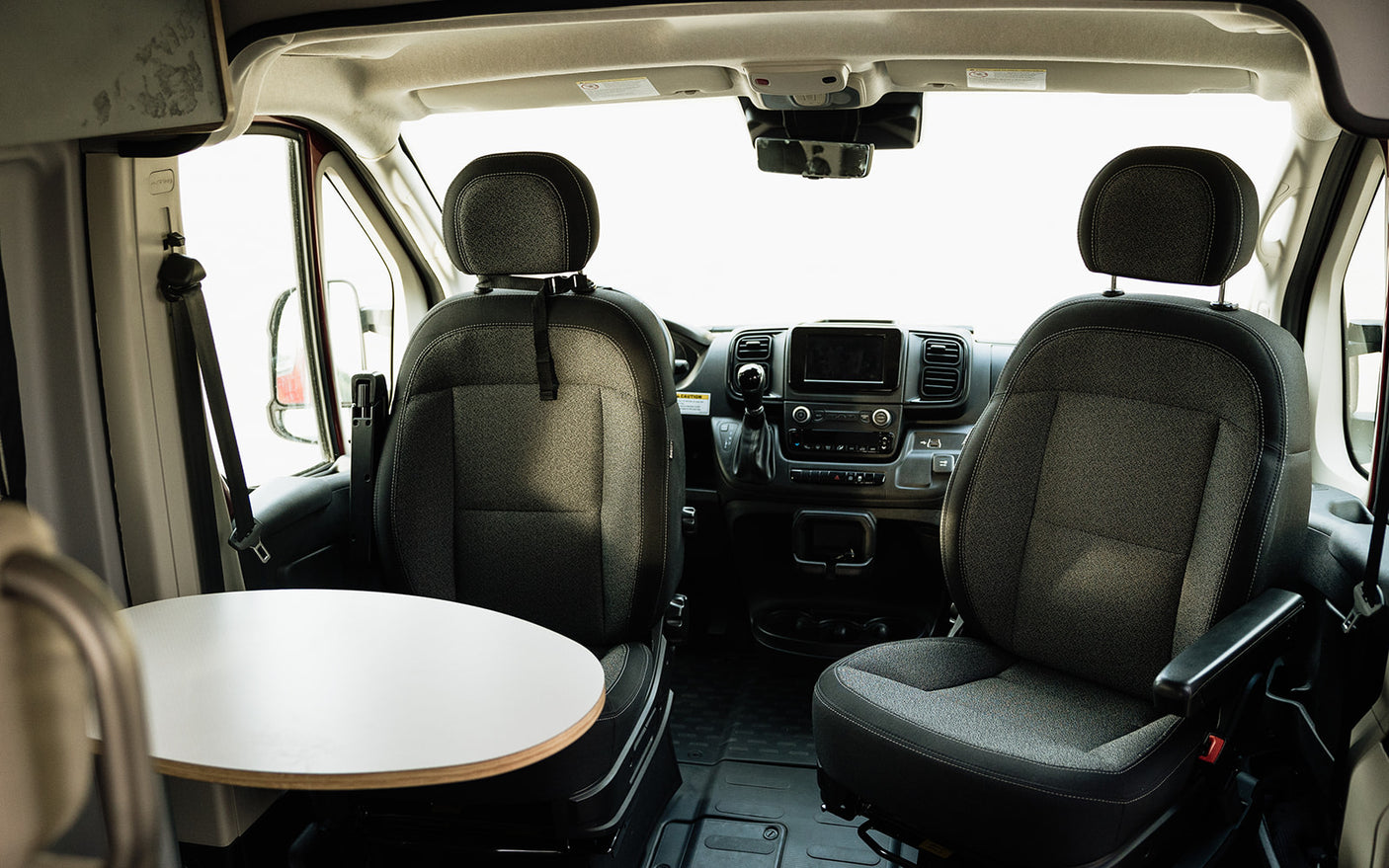 Spacious RV rental interior: front cabin with swiveling seats, dashboard, and a small table, ideal for van life adventurers.