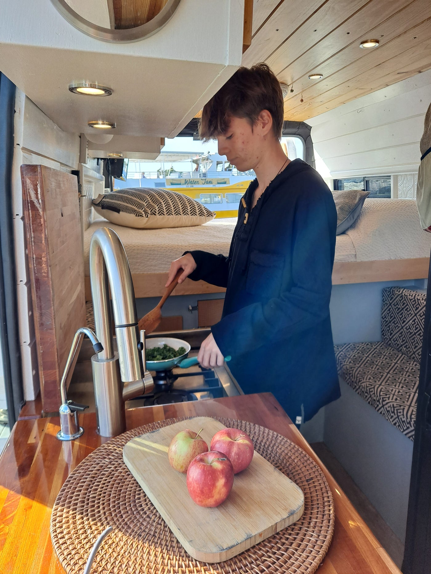 A person cooks in a modern RV rental, featuring a compact kitchen with wood accents and a cozy bed area. — photo 16