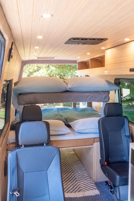 RV rental interior with cozy bunk beds, wood-paneled ceiling lights, and passenger seating. Perfect for families.