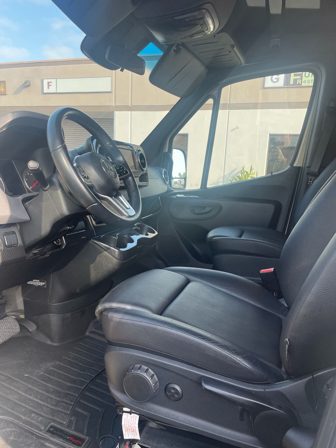 Interior of a Mercedes-Benz Sprinter van, ideal for rv rental. Shows black leather seats, steering wheel & WeatherTech mats.
