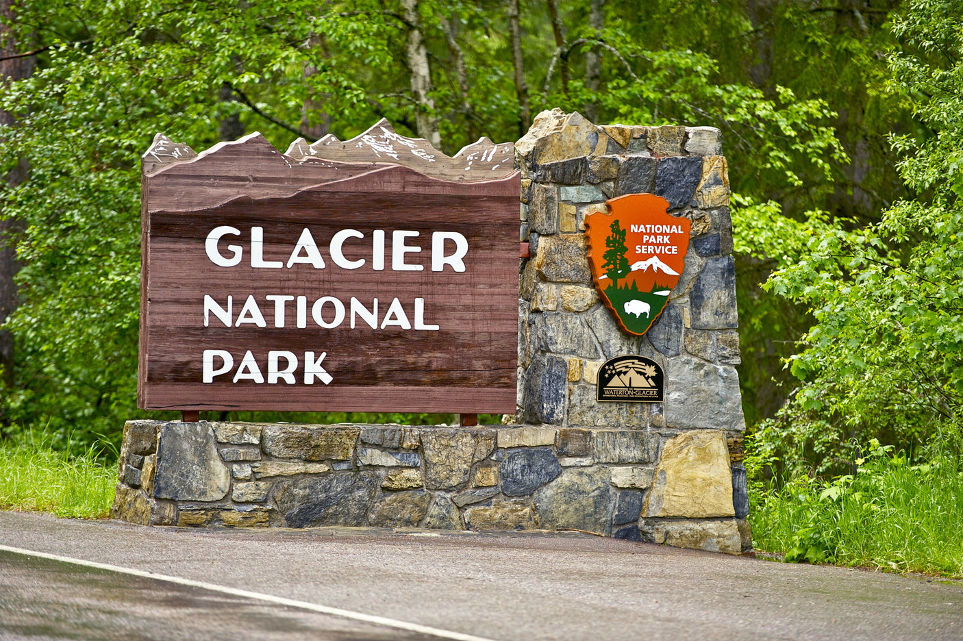 Glacier National Park entrance sign, a perfect RV rental destination. Lush greenery frames the stone base.