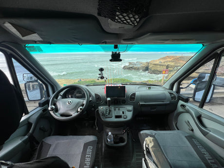 RV rental interior: driver's seat view of a stunning ocean vista from a Mercedes van. Coastal cliffs and dashboard visible.