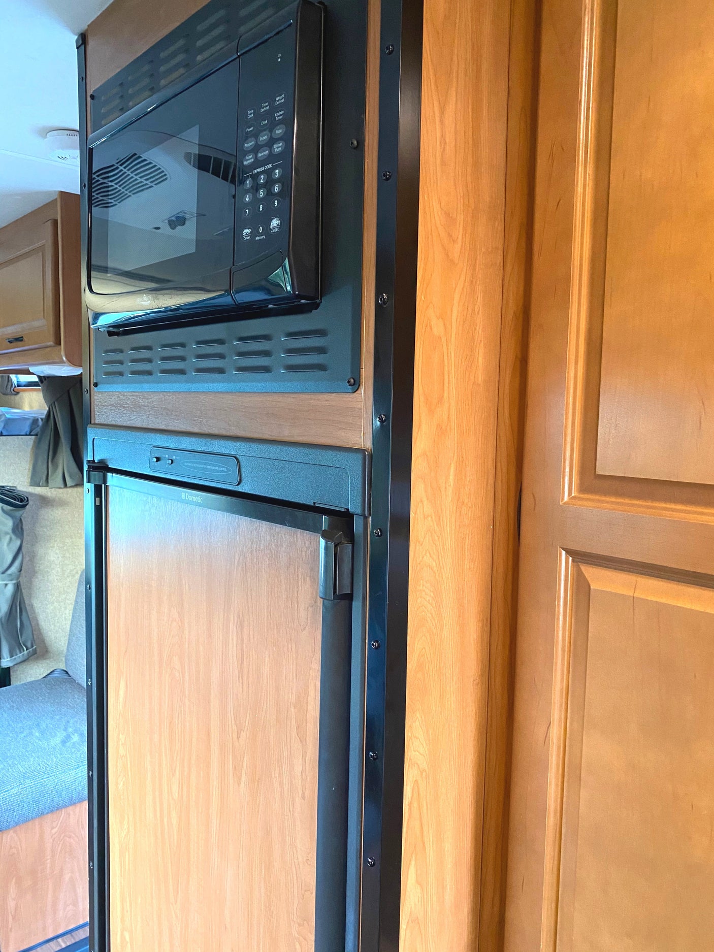 Inside an RV rental: compact microwave above Dometic refrigerator with wood finishes.