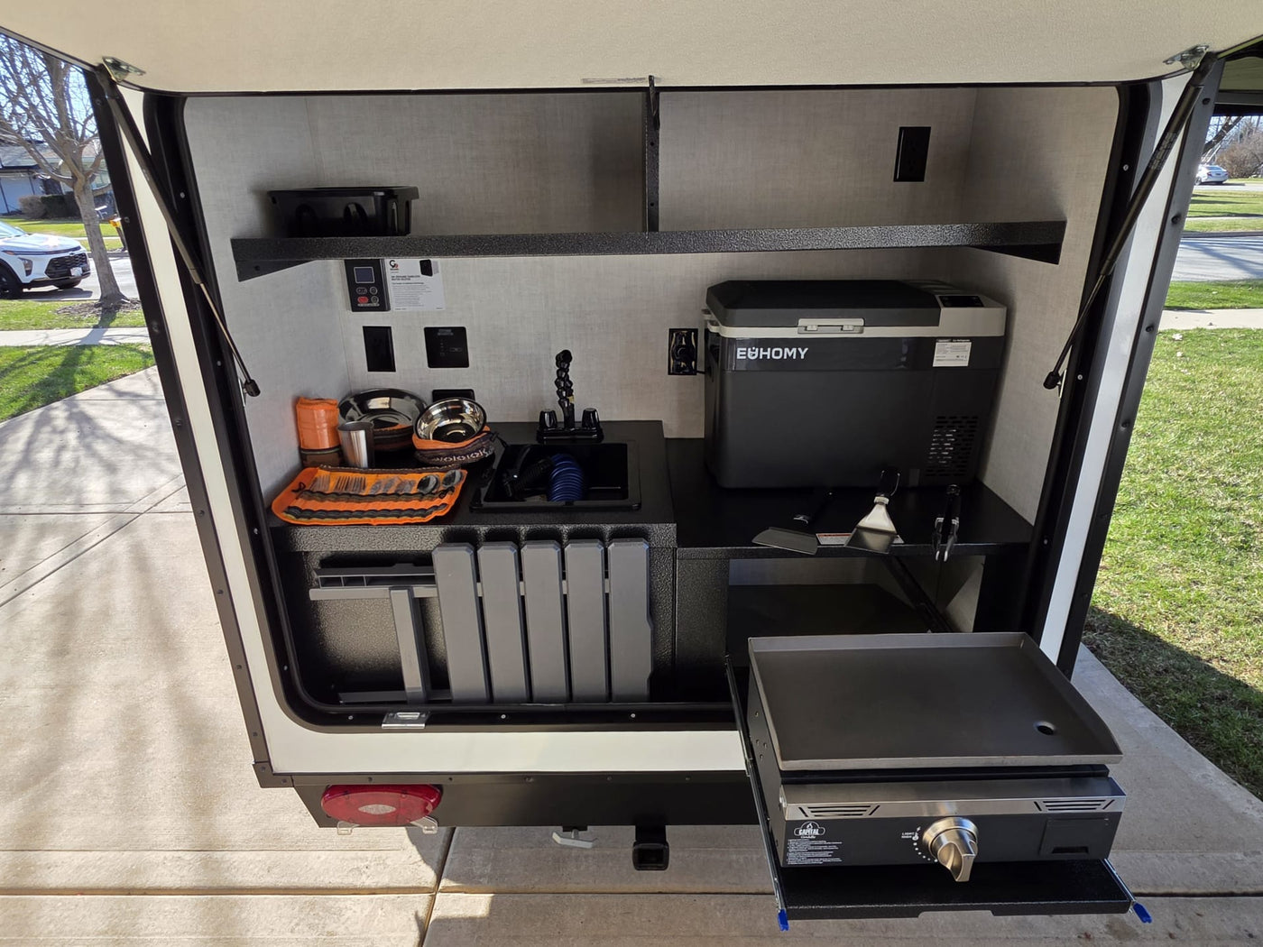 An RV rental's side compartment reveals a well-equipped outdoor kitchen with a sink, fridge, and griddle. — photo 13