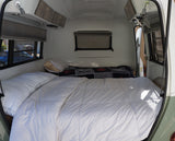 Compact rv rental bedroom with a comfy bed, white duvet, pillows, overhead cabinets, and windows with blinds. Ideal for travel.