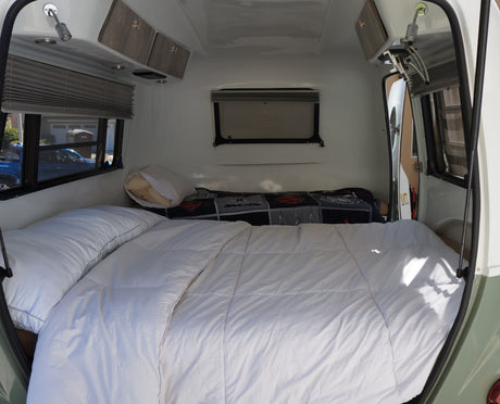 Compact rv rental bedroom with a comfy bed, white duvet, pillows, overhead cabinets, and windows with blinds. Ideal for travel.