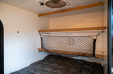 Cozy RV rental interior with a bed, overhead shelf, and practical cargo net storage.