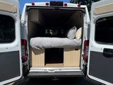 Rear view of an RV rental camper van, revealing its cozy bed, pillows, and built-in wooden storage. Ready for adventure.