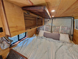 Step inside this cozy RV rental's wooden interior, featuring a comfy bed, overhead storage, and warm lighting.