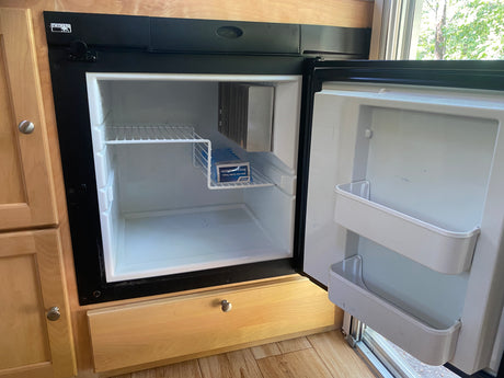 Inside an RV rental: a compact Norcold refrigerator, open to show its white interior, shelves, and ice cube trays.