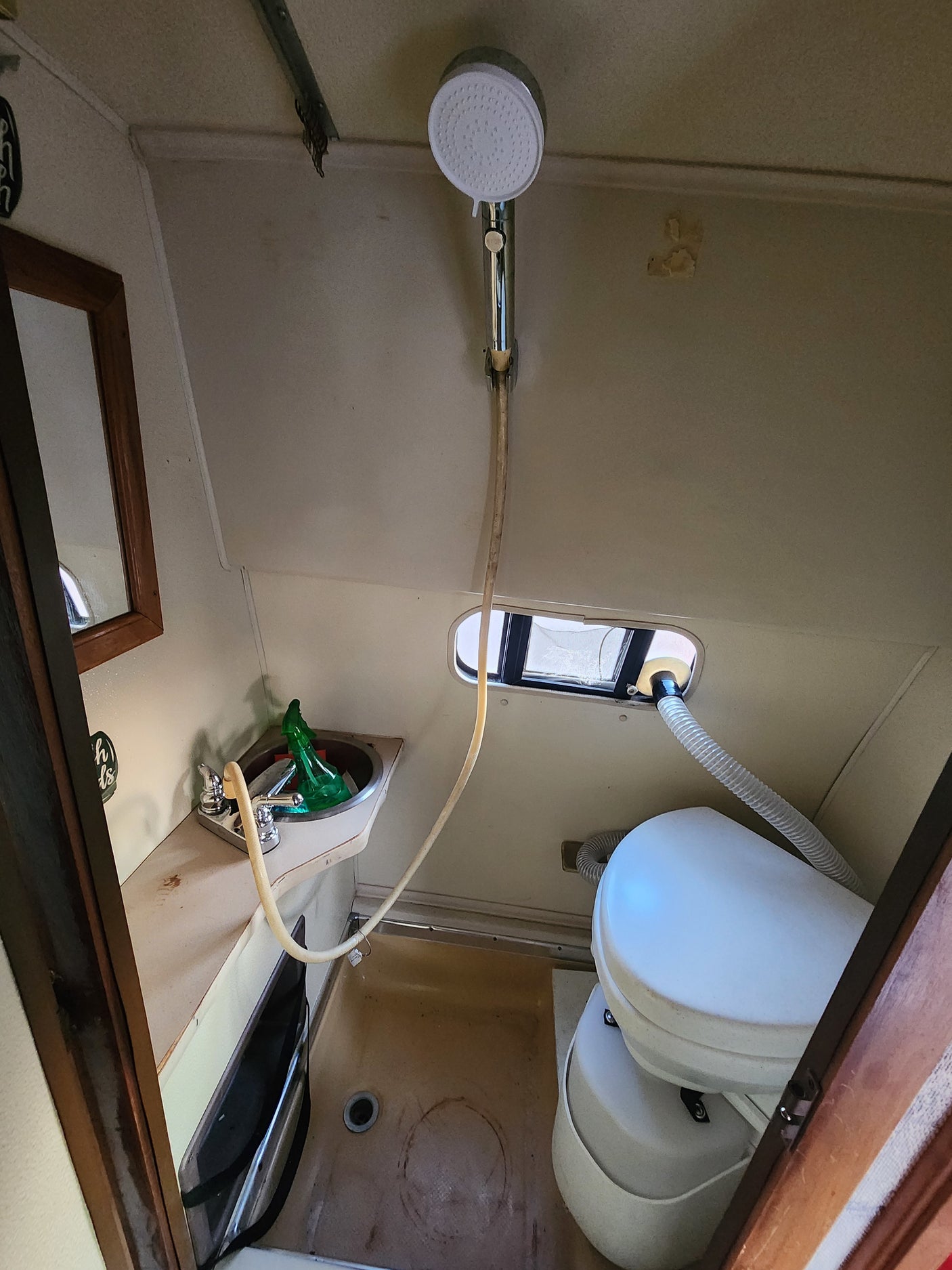 Compact RV rental bathroom with a sink, handheld shower, window, and composting toilet inside.