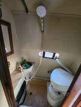 Compact RV rental bathroom with a sink, handheld shower, window, and composting toilet inside.