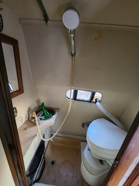 Compact RV rental bathroom with a sink, handheld shower, window, and composting toilet inside.