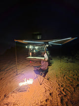 Night desert scene: an rv rental overland setup with illuminated awning, cozy campfire, and camping chair ready.