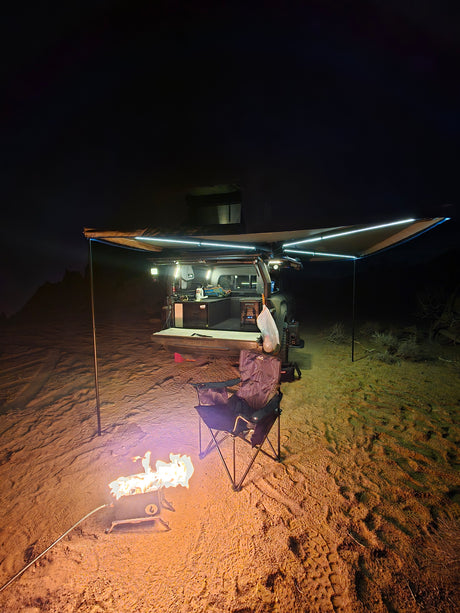 Night desert scene: an rv rental overland setup with illuminated awning, cozy campfire, and camping chair ready.