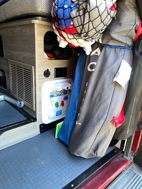 Inside an RV rental: a utility panel for water hookups (city/tank) and an outlet, alongside mesh storage for camping gear.