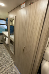 Compact RV rental interior featuring a stylish wardrobe with integrated mirror, counter space, and a scenic window view.