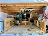 Rear interior of a DIY van conversion, ideal for an RV rental. Features rustic wood framing, storage, and an overhead table.