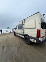 This RV rental Sprinter van, equipped for adventure, is parked on a sandy beach overlooking the ocean.