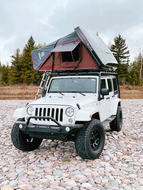White Jeep Wrangler with a rooftop tent on a rocky riverbed. Your ideal RV rental for outdoor adventures!