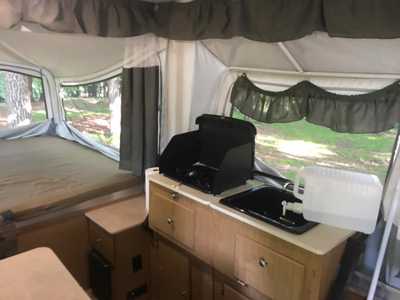 Inside a spacious pop-up camper for your next rv rental adventure. Features a comfy bed, kitchen with stove, and sink. — photo 8