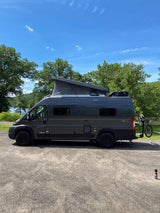 Dark grey Winnebago Solis camper van, pop-top extended, bike on rear rack. Ideal rv rental by the lake.