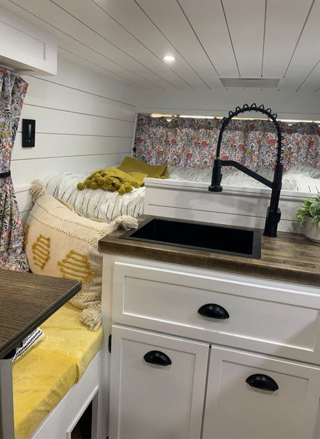 RV rental: Bright, modern interior featuring a cozy bed, shiplap walls, and compact kitchen with a black sink and wood counter.