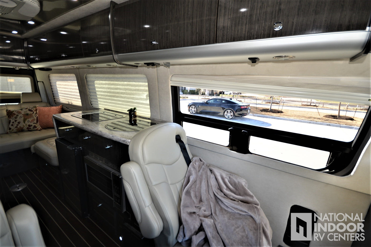 Step inside this luxury rv rental, featuring a modern kitchen, plush seating, and a clear view out to a black Camaro.