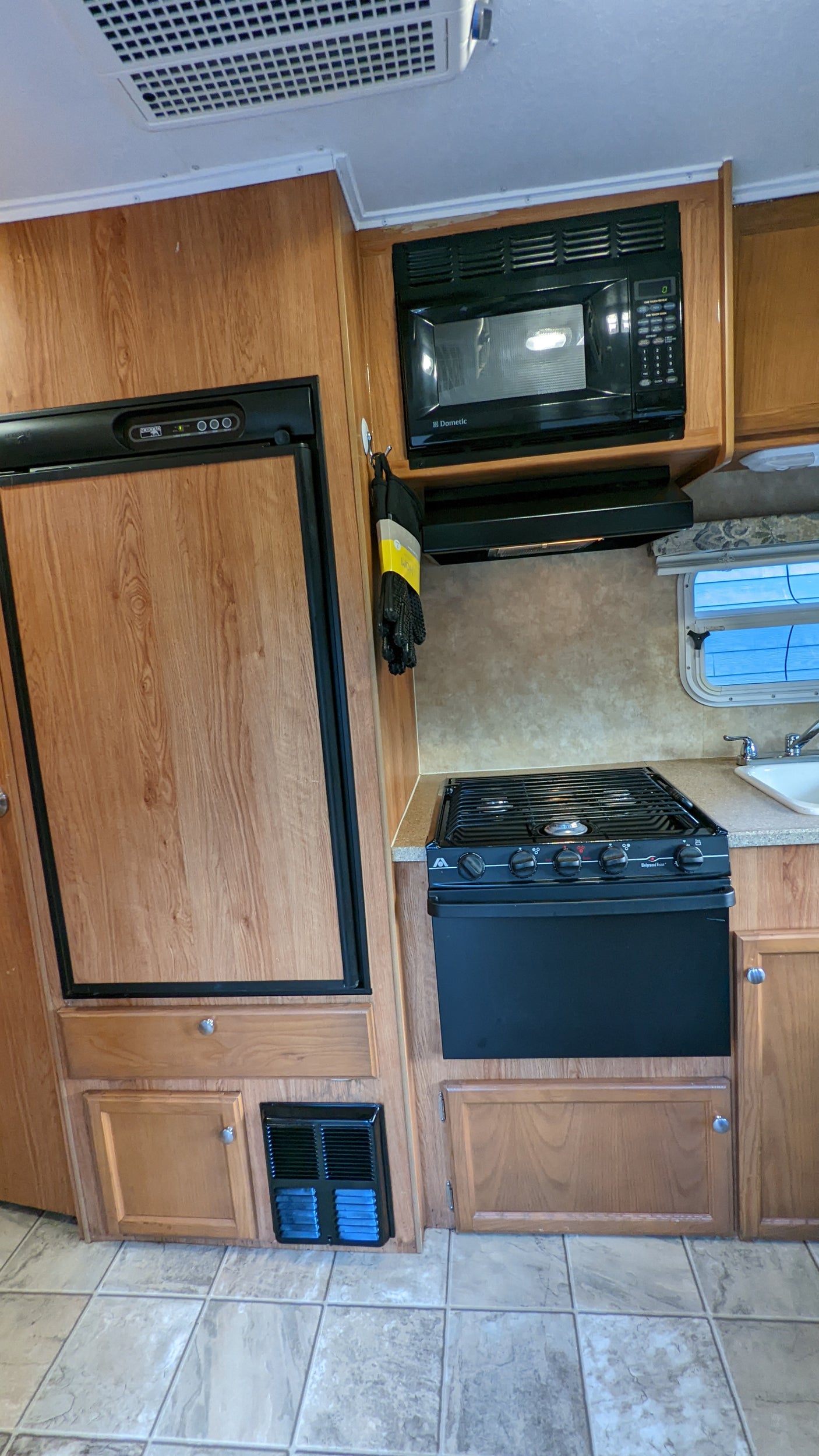 RV rental kitchen: This interior view shows a wood-look refrigerator, black microwave, and stove with a sink and tiled floor.