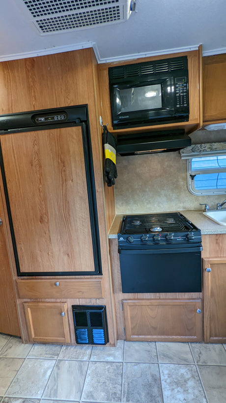 RV rental kitchen: This interior view shows a wood-look refrigerator, black microwave, and stove with a sink and tiled floor.