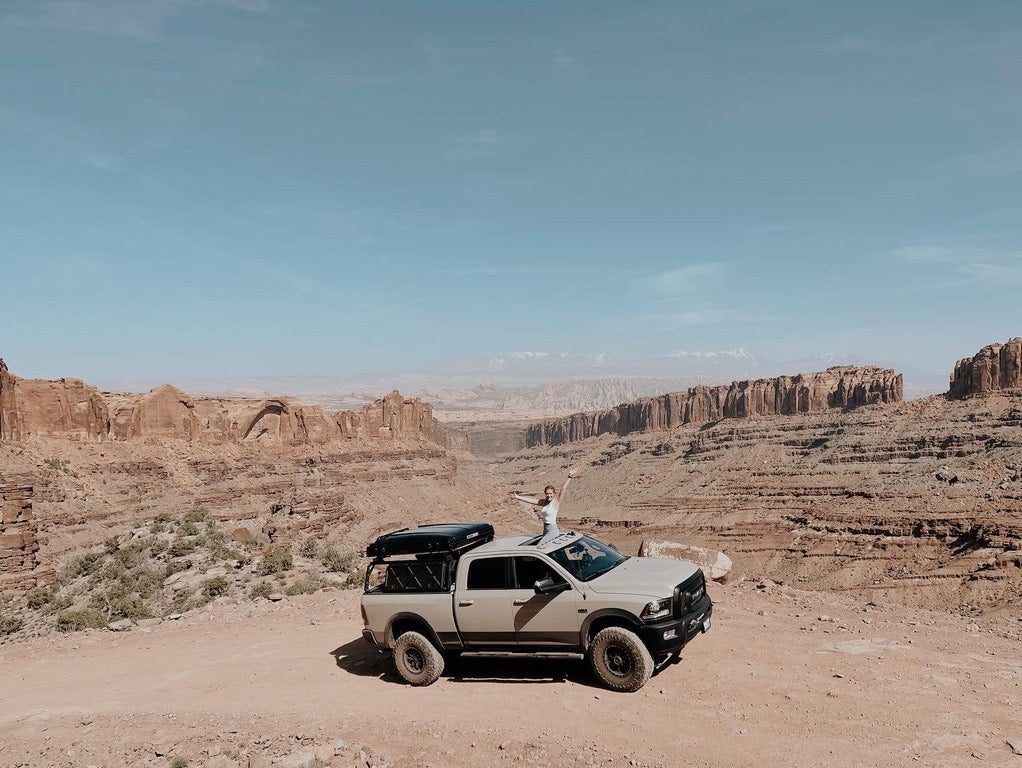 Thrilled traveler atop an adventure truck in vast desert canyons. Experience the freedom of RV rental exploration!