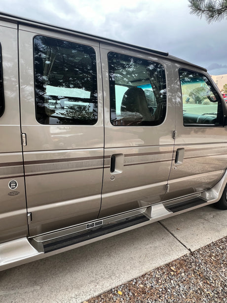 Side view of a beige RV rental van, showing its windows, passenger doors, and running boards. Ideal for road trips.
