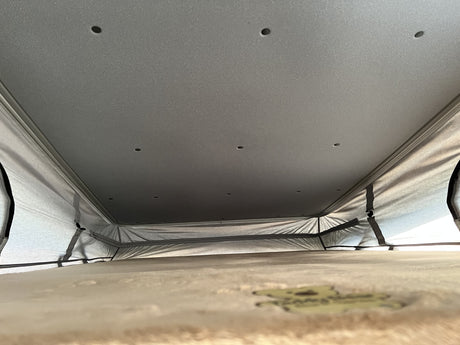 Inside an RV rental pop-top camper, showing the ceiling lights, fabric walls, and elevated sleeping platform for a cozy experience.
