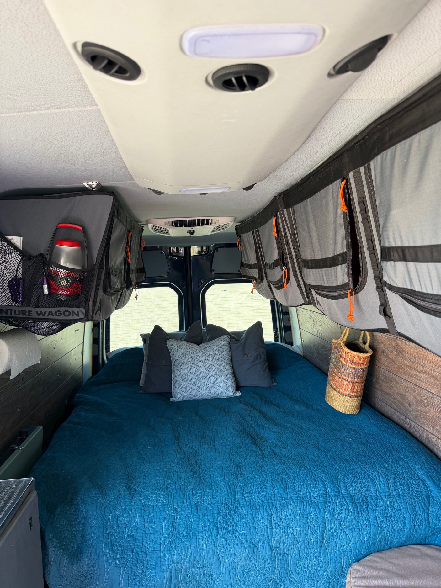 RV rental: cozy bed with blue quilt & pillows, ample overhead storage, and ceiling AC for comfortable travel.