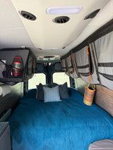 RV rental: cozy bed with blue quilt & pillows, ample overhead storage, and ceiling AC for comfortable travel.