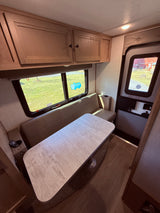 Spacious RV rental interior featuring a bright dinette area with bench seating, overhead cabinets, and large windows.