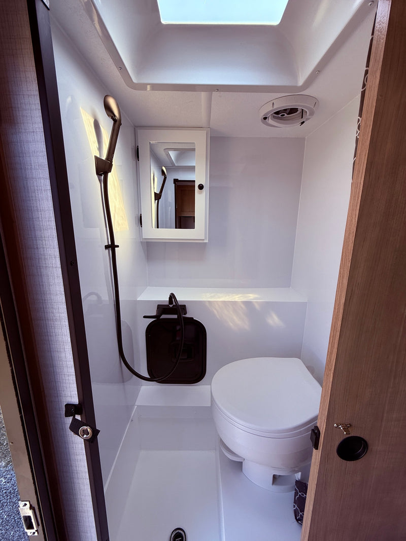 Bright, compact RV wet bath for rv rental, featuring a shower, toilet, mirrored cabinet, and ceiling skylight. — photo 7