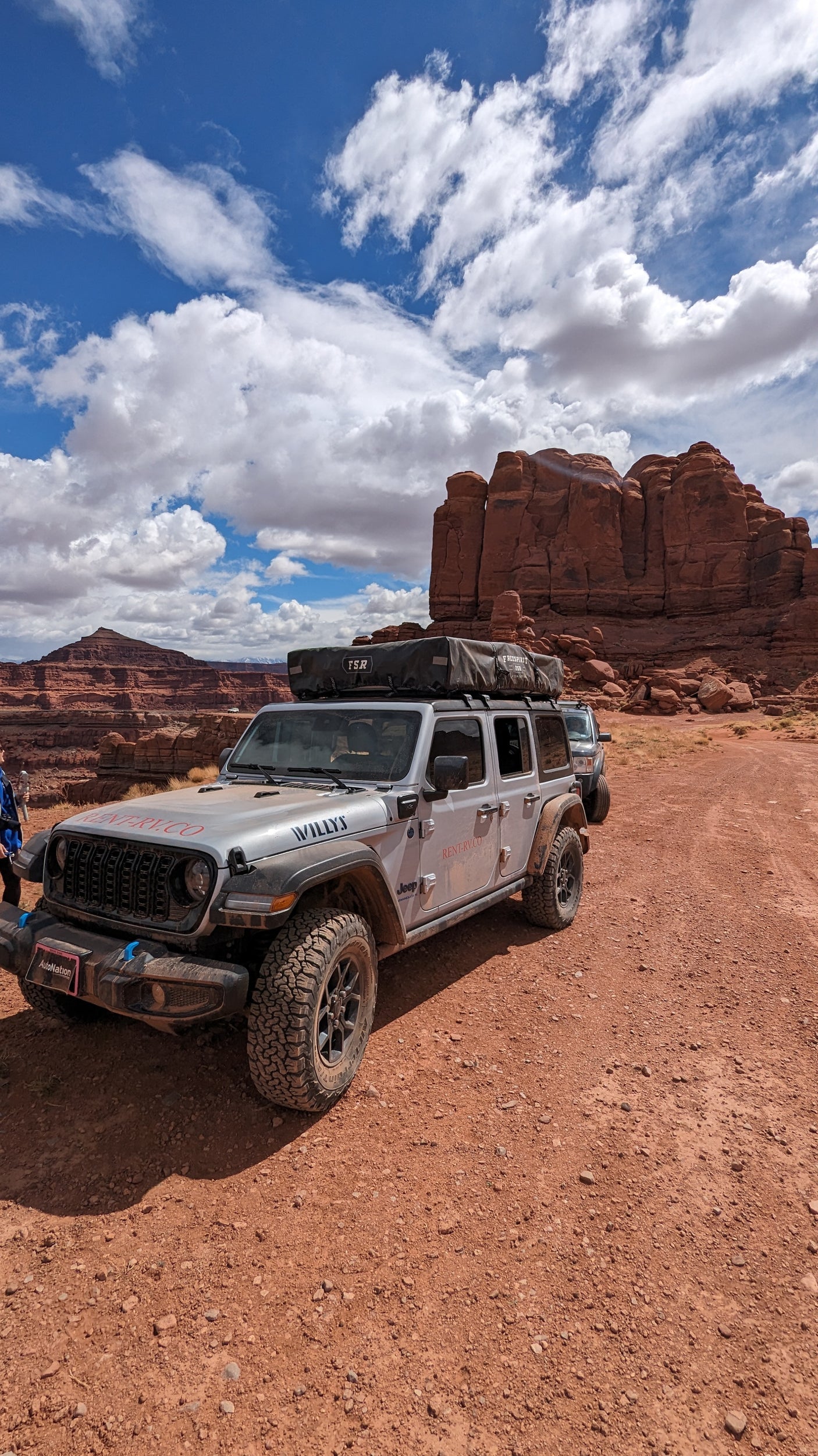 An RV rental Jeep Willys, with a rooftop tent, explores a stunning red rock desert landscape.