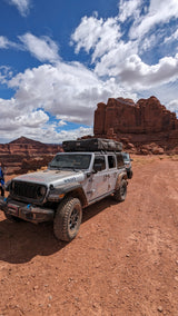 An RV rental Jeep Willys, with a rooftop tent, explores a stunning red rock desert landscape.