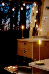 Serene RV rental interior at night, illuminated by modern lamps, string lights, and soft candles. Wood details.
