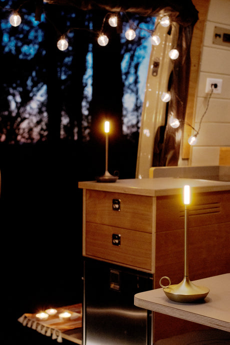 Serene RV rental interior at night, illuminated by modern lamps, string lights, and soft candles. Wood details.