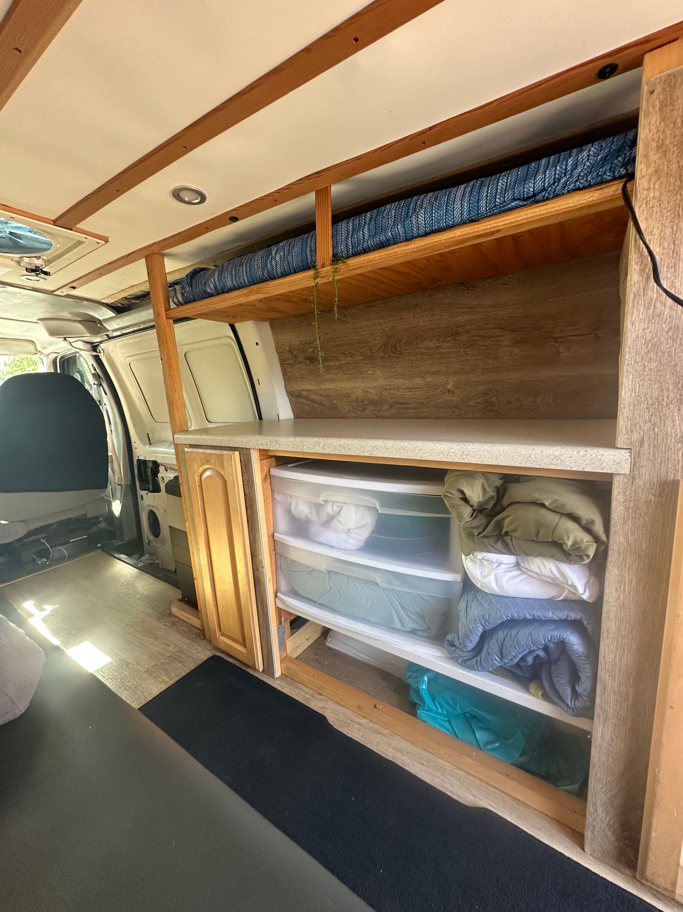 This RV rental showcases a functional van interior with custom wood shelving, a compact bed, a countertop, and clear storage drawers.