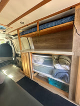 This RV rental showcases a functional van interior with custom wood shelving, a compact bed, a countertop, and clear storage drawers.