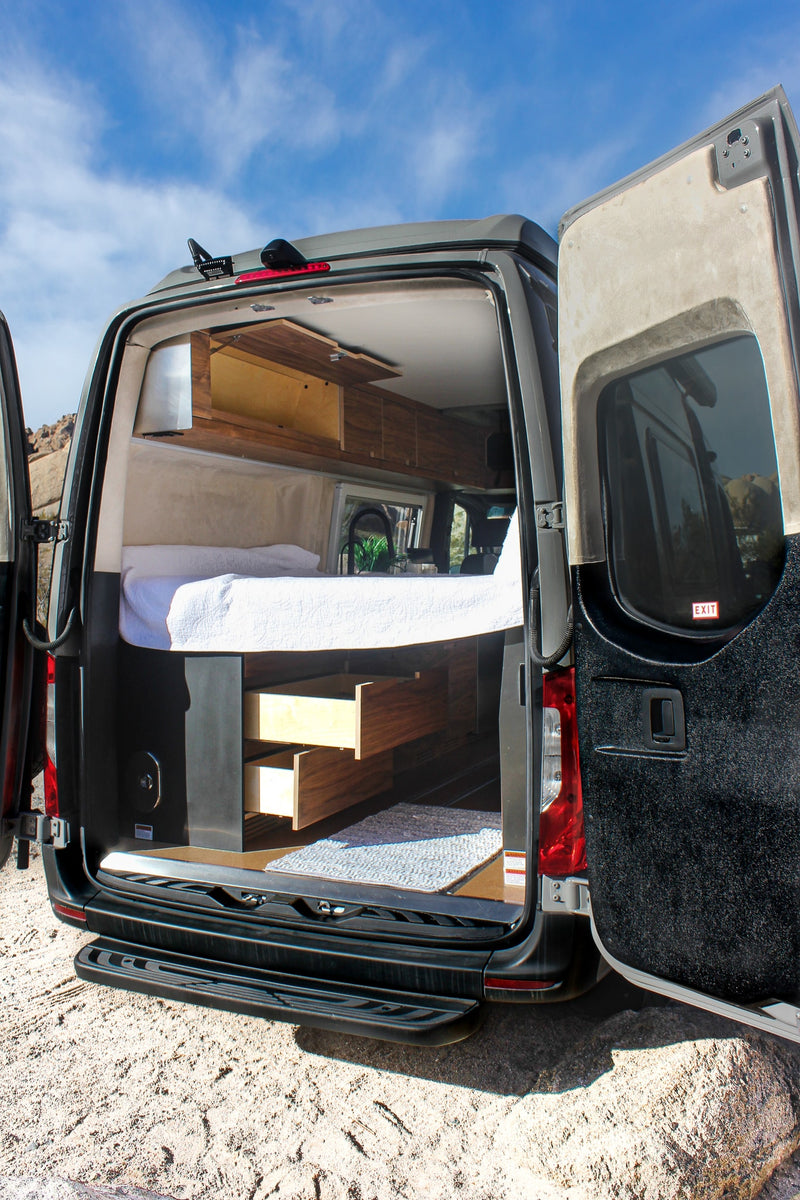 Inside an RV rental: a modern camper van with open rear doors, revealing a comfy bed, pull-out storage, and wooden interior. — photo 11