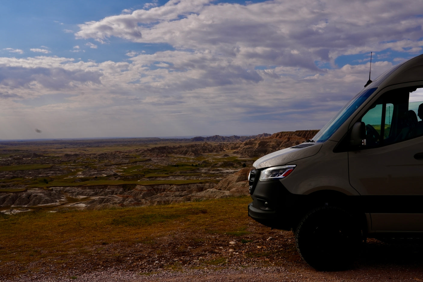 Experience epic views with an **RV rental**! A camper van overlooks a vast badlands landscape under a cloud-filled sky.